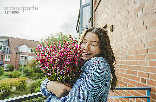 Glückliches Teenager-Mädchen hält Heideblumen auf dem Balkon