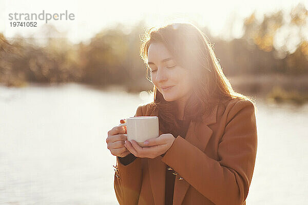 Glückliche Frau hält eine Tasse Tee in der Nähe des Sees
