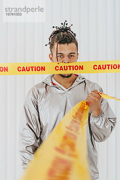Young man with mouth covered gripping restriction tape in front of wall