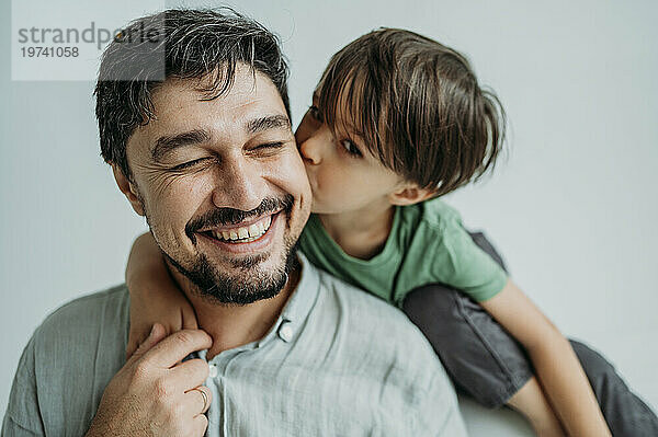 Sohn küsst glücklichen Vater auf Wangen vor weißem Hintergrund