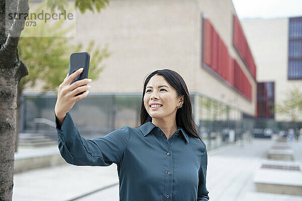 Glückliche Geschäftsfrau  die vor dem Gebäude ein Selfie mit dem Smartphone macht