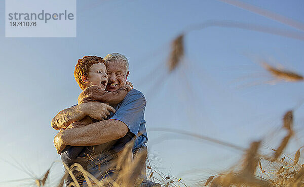 Lächelnder Großvater umarmt Enkel unter freiem Himmel