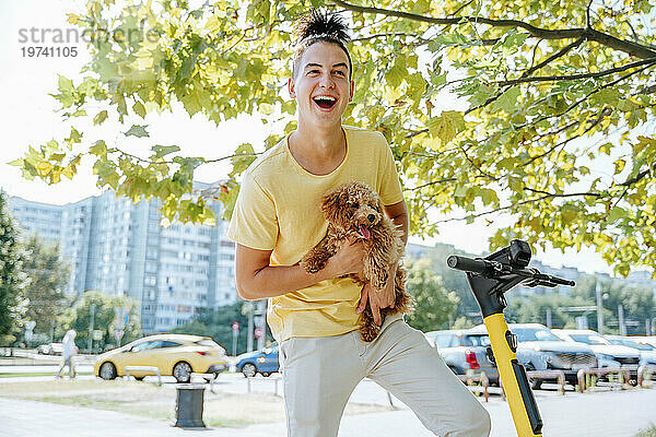 Lächelnder Mann mit Hund auf Tretroller in der Stadt