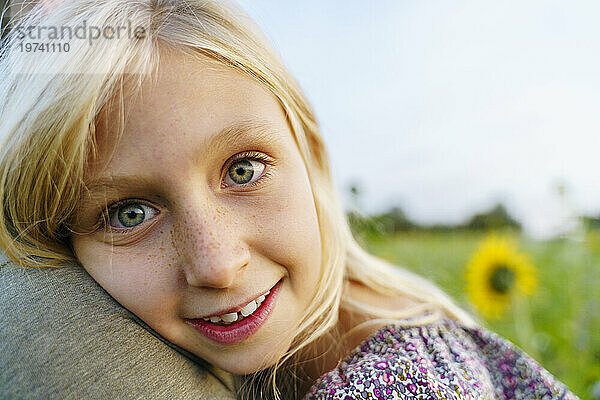 Smiling blond girl leaning on father in field