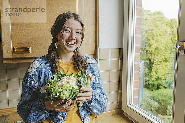 Glückliches Teenager-Mädchen hält Blumenkohl am Fenster zu Hause