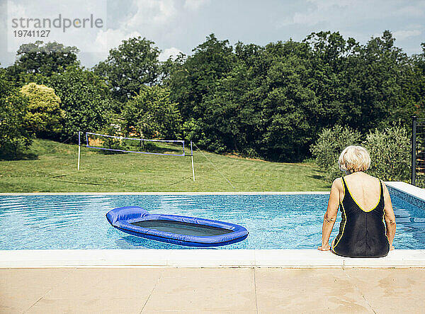 Ältere Frau in Badebekleidung sitzt am Pool
