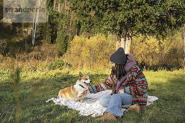 Junge Frau macht am Wochenende Handschlag mit Hund auf Decke im Naturpark