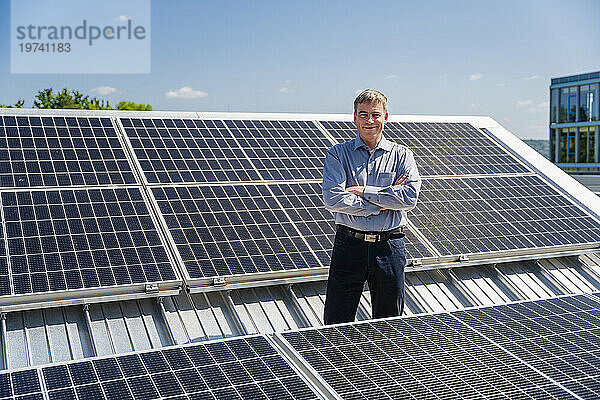 Ein selbstbewusster Geschäftsmann steht stolz umgeben von Reihen glänzender Solarpaneele