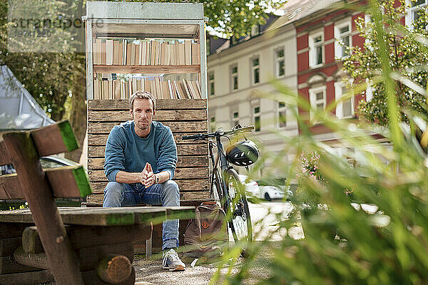 Mann sitzt auf Bank neben Bücherschrank in der Nähe von Pflanzen