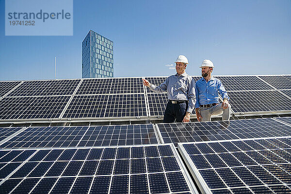 Zwei Geschäftsleute in Schutzhelmen diskutieren über die Installation von Solarmodulen