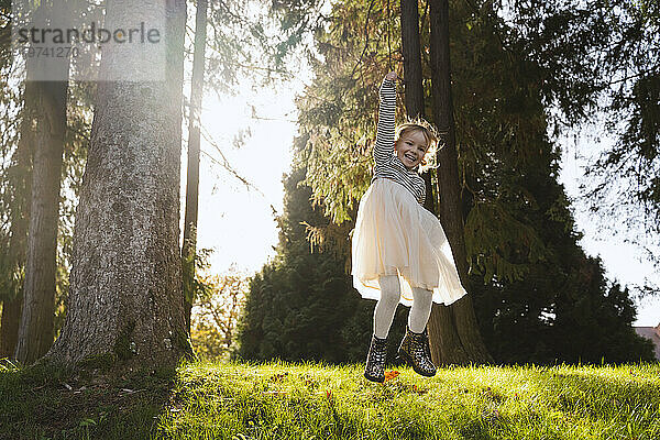 Cheerful girl jumping near trees in forest on sunny day