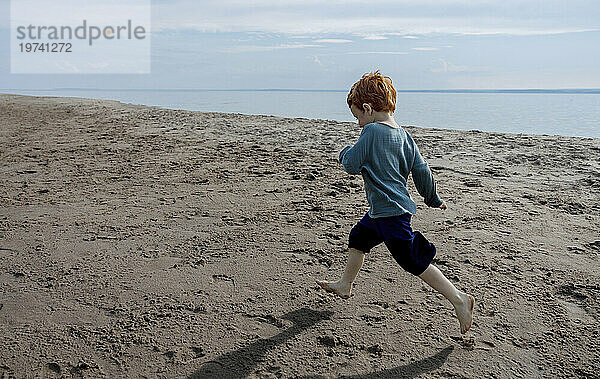 Verspielter Junge läuft am Strand auf Sand