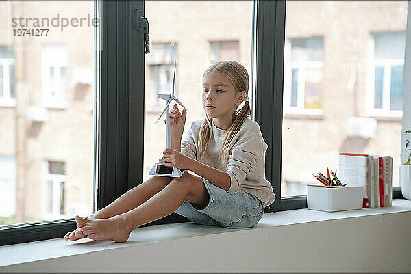 Blonde Frau spielt mit Windturbinenmodell auf Fensterbank zu Hause