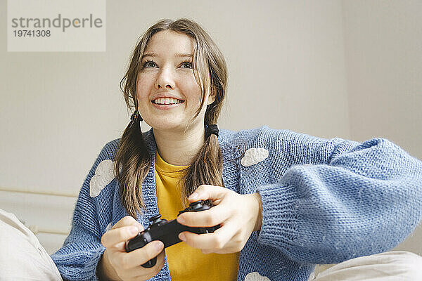 Happy girl playing video game with controller in bedroom at home