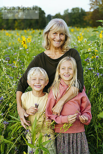 Großmutter steht mit Enkel und Enkelin im Sonnenblumenfeld
