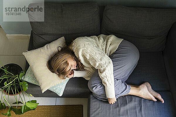 Frau mit Bauchschmerzen schläft zu Hause auf dem Sofa