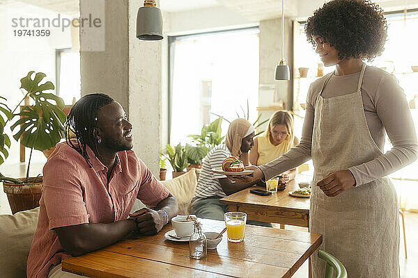 Lächelnde Kellnerin serviert Kunden im Café Croissants