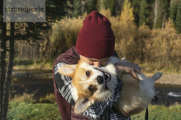 Mann mit Strickmütze küsst am Wochenende glücklichen Hund im Park