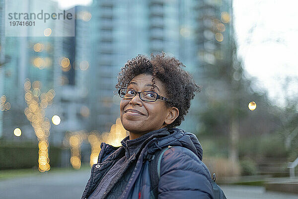 Nahaufnahmeporträt einer Frau  die in der Dämmerung draußen in Vancouver steht  lächelt und nach oben schaut; Vancouver  British Columbia  Kanada