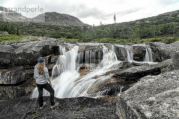 Blick von hinten auf eine Frau  die auf einer felsigen Klippe über den Wasserfällen entlang des International Falls Trail steht  einer der großartigsten Wanderungen im Yukon-Gebiet; Yukon  Kanada