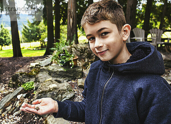 Nahaufnahmeporträt eines kleinen Jungen  der im Urlaub in die Kamera lächelt und einen kleinen Frosch in der Hand hält; Sicamous  British Columbia  Kanada