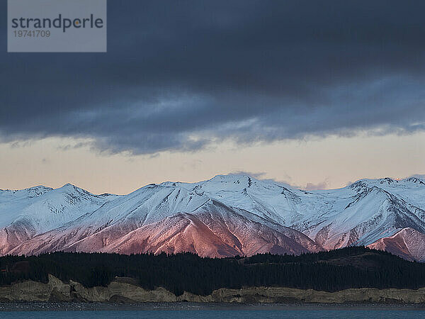 Das Morgenlicht beleuchtet die schneebedeckten Rhoboro Hills mit einem ruhigen Lake Pukaki im Vordergrund; Twizel  Südinsel  Neuseeland