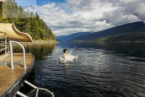 Junge planscht ins Wasser  nachdem er an einem Herbsttag auf dem Shuswap Lake aus dem Ende einer Hausboot-Wasserrutsche gerutscht ist; British Columbia  Kanada