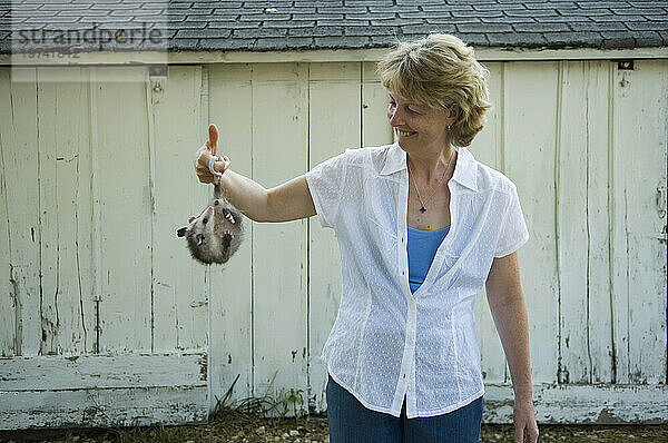 Frau steht auf einem Bauernhof und hält ein Opossum (Didelphis virginiana) am Schwanz; Greenleaf  Kansas  Vereinigte Staaten von Amerika