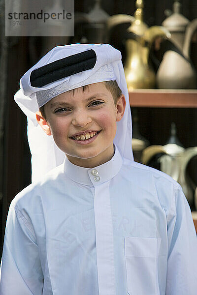 Nahaufnahme eines jungen arabischen Jungen in traditioneller Kleidung  der auf dem Souq Waqif-Marktplatz in Doha in die Kamera lächelt; Doha  Katar