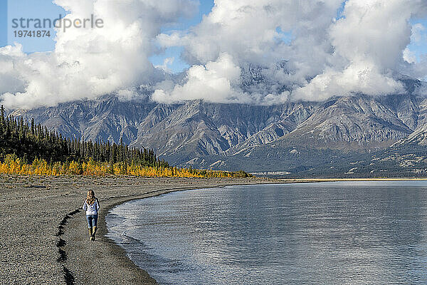 Frau spaziert am Ufer des Kluane Lake  umgeben von Bergen. Eine unglaublich schöne Szene; Yukon  Kanada