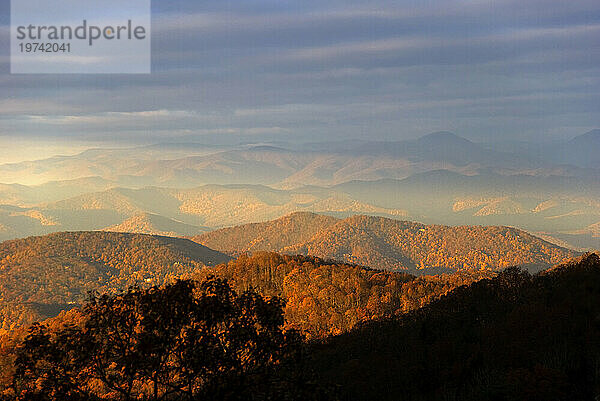 Das Sonnenlicht des frühen Morgens beleuchtet die Herbstfarben über den Blue Ridge Mountains mit einem dunstigen  bewölkten Himmel; North Carolina  Vereinigte Staaten von Amerika