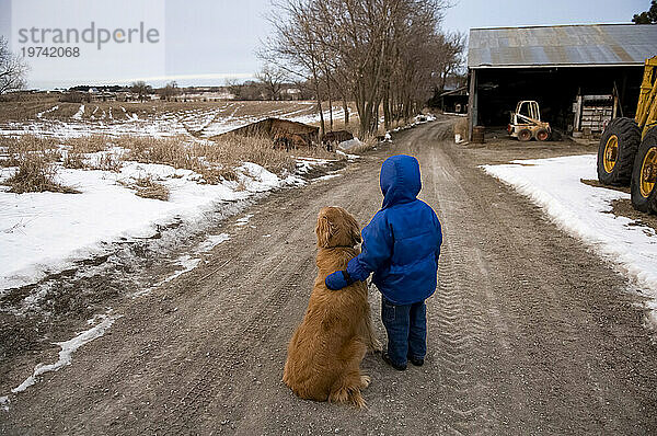 Kleiner Junge steht mit einem Golden Retriever auf einer Schotterstraße; Cortland  Nebraska  Vereinigte Staaten von Amerika