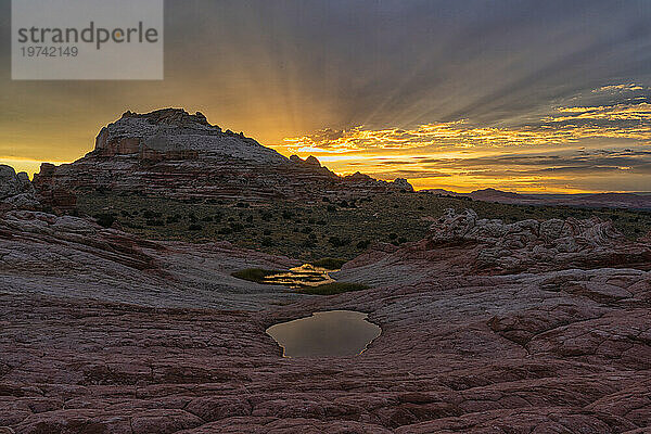 Sonnenuntergang mit Dämmerungsstrahlen über der wundersamen Gegend  die als White Pocket in Arizona bekannt ist. Es ist eine fremde Landschaft mit erstaunlichen Linien  Konturen und Formen. Hier erzeugt die untergehende Sonne wunderschöne Farben am Himmel über der Gegend; Arizona  Vereinigte Staaten von Amerika