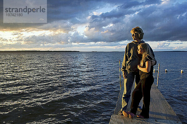 Mutter und ihre Tochter stehen auf einem Bootssteg und beobachten den Sonnenuntergang  Leech Lake in Minnesota  USA; Walker  Minnesota  Vereinigte Staaten von Amerika