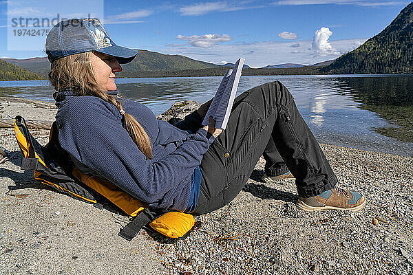 Eine Frau  die ihr bestes Leben führt und ein Buch am Ufer eines abgelegenen Yukon-Sees liest; Yukon  Kanada