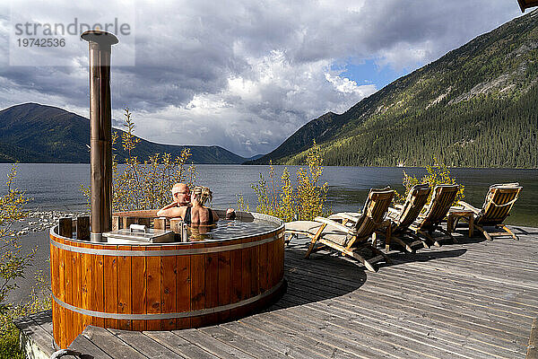 Paar teilt einen zärtlichen Moment  während es in einem holzbefeuerten Whirlpool am Ufer eines Yukon-Sees sitzt; Yukon  Kanada