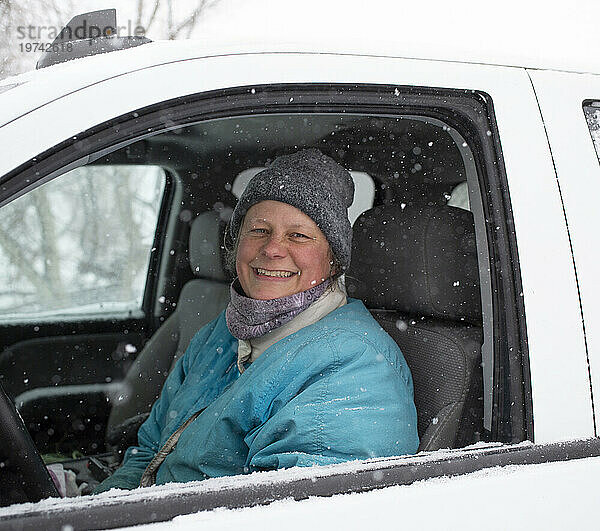 Nahaufnahme einer Bäuerin  die in Winterkleidung auf dem Fahrersitz eines Autos sitzt und in die Kamera lächelt  während im Winter Schneeflocken fallen; Ottawa Valley  Ontario  Kanada