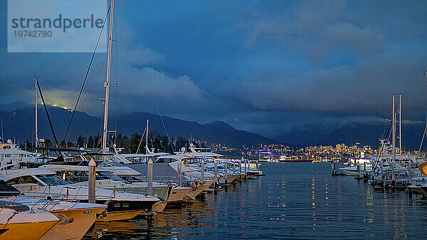 Malerischer Blick auf Boote  die im Jachthafen festgemacht haben  mit Blick auf die Stadt im Hintergrund an der Uferpromenade des Hafens von Vancouver in der Dämmerung; Vancouver  British Columbia  Kanada