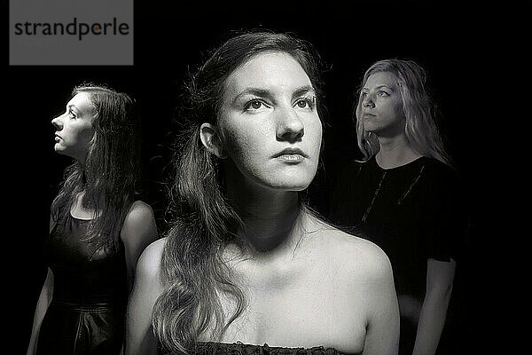 Drei junge Frauen in Abendgarderobe blicken vor schwarzem Hintergrund nach oben; Studio