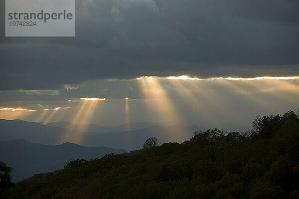 Sonnenlicht strömt in der Dämmerung durch Lücken in den grauen Wolken über den Blue Ridge Mountains; North Carolina  Vereinigte Staaten von Amerika