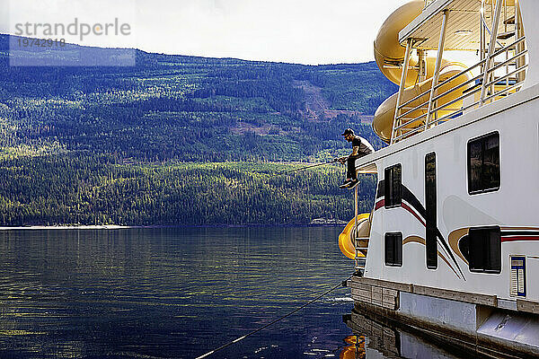 Mann genießt einen Familienurlaub  einen Hausbooturlaub und angelt vom Deck des Hausboots aus  während er am Ufer des Shuswap Lake parkt; Shuswap Lake  British Columbia  Kanada