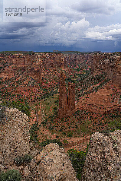 Überblick über den Canyon de Chelly mit der als Spider Rises bekannten Felsformation  die aus dem Canyon ragt  Talboden umgeben von der erodierten roten Felslandschaft unter stürmischem Himmel; Arizona  Vereinigte Staaten von Amerika