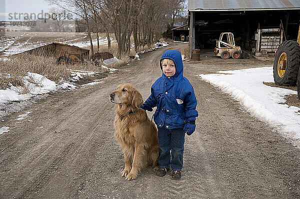 Kleiner Junge steht mit einem Golden Retriever auf einer Schotterstraße; Cortland  Nebraska  Vereinigte Staaten von Amerika