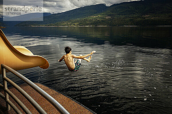 Junge springt an einem Herbsttag auf dem Shuswap Lake aus dem Ende einer Wasserrutsche auf einem Hausboot; British Columbia  Kanada