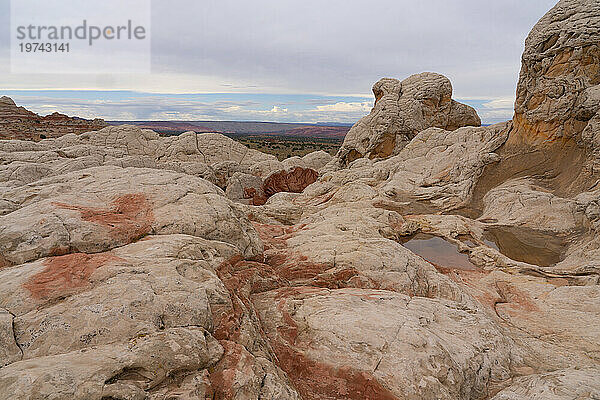 Malerische Aussicht auf Felsformationen mit dem Plateau in der Ferne unter einem bewölkten Himmel  die Teil der fremden Landschaft mit erstaunlichen Linien  Konturen und Formen in der wundersamen Gegend namens White Pocket in Arizona sind; Arizona  Vereinigte Staaten von Amerika