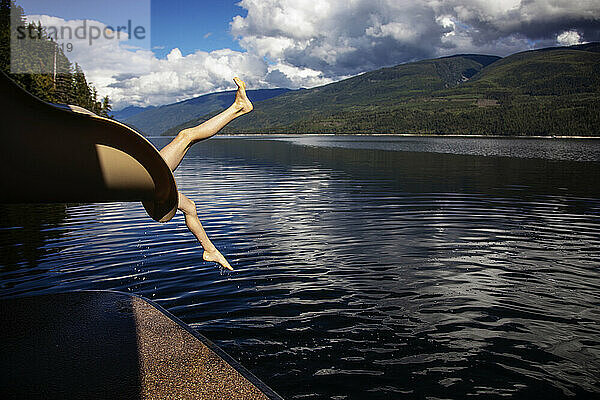 Die Beine eines Jungen erscheinen am Ende einer Hausboot-Wasserrutsche  als er in den Shuswap Lake rutscht; British Columbia  Kanada