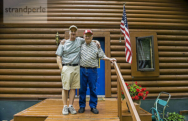 Vater und Sohn stehen mit amerikanischer Flagge vor ihrer Hütte; Cross Lake  Minnesota  Vereinigte Staaten von Amerika