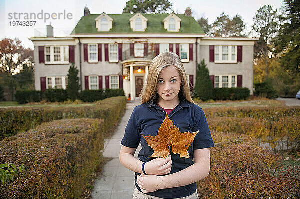 Teenager-Mädchen vor ihrem Haus hält ein großes herbstlich gefärbtes Blatt; Lincoln  Nebraska  Vereinigte Staaten von Amerika