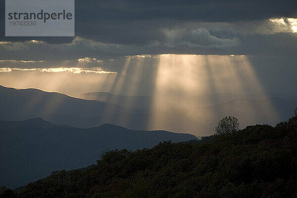 Sonnenlicht strömt in der Dämmerung durch Lücken in den grauen Wolken über den Blue Ridge Mountains; North Carolina  Vereinigte Staaten von Amerika