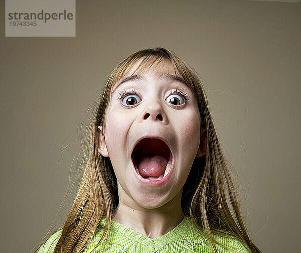 Junges Mädchen öffnet den Mund weit und zeigt der Kamera einen aufgeregten Ausdruck; Studio